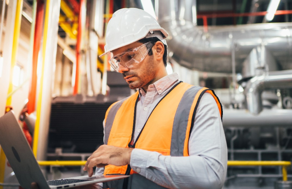 Man working in energy plant with laptop and protective wear